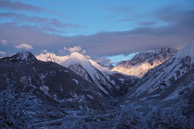 Snow-covered mountains catching pink dawn light above a dark valley