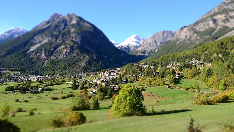 Green Valtellina valley meadows with Bormio nestled below snow-dusted alpine peaks