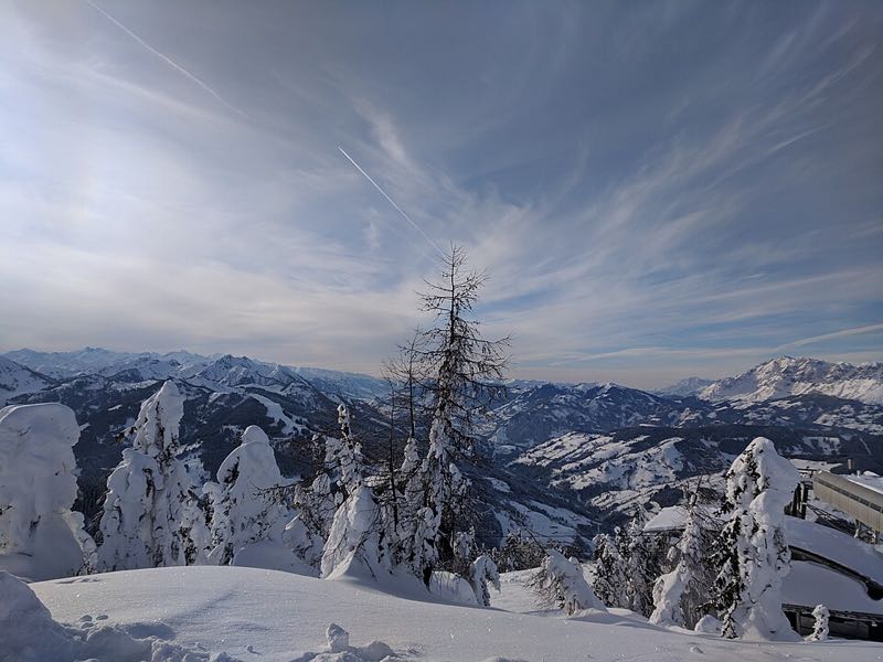 Snow-laden trees on a Flachau ridge overlooking a deep white valley and distant alpine peaks