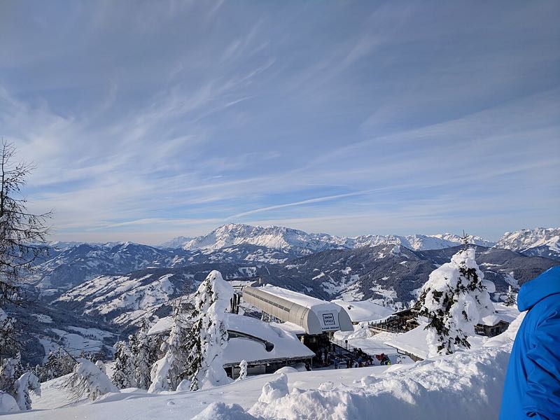Winter summit view above Flachau with a mountain-top lift station and snowy peaks under blue sky