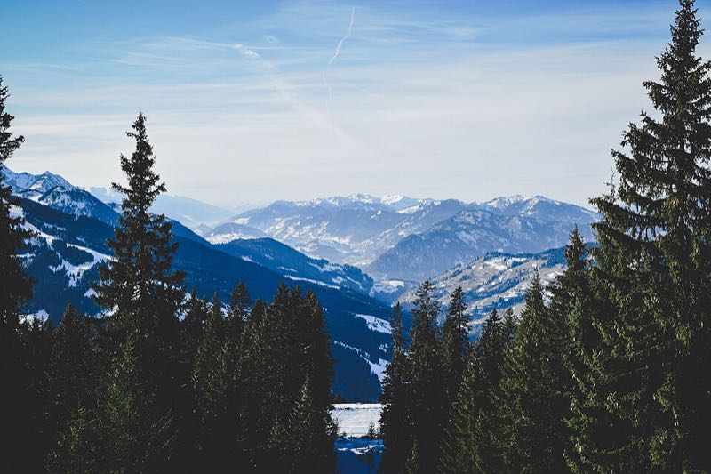 Winter view framed by snowy conifers looking down the Flachau valley to distant snow-covered ranges