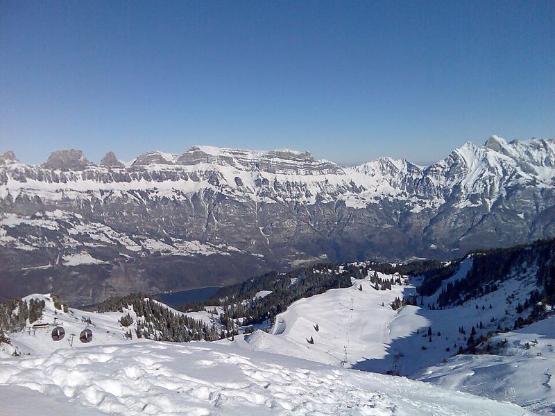 Snow-covered ski slopes and a gondola line below the Churfirsten cliffs, with the Walensee in the valley