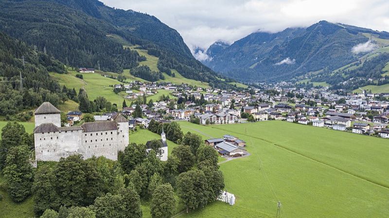 Aerial drone view of Kaprun village nestled in its green valley with snow-capped mountains behind