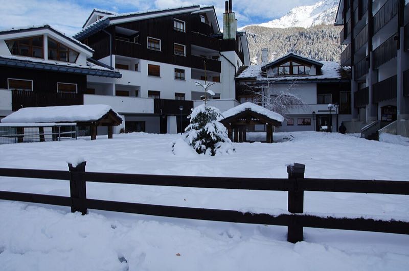 Chalets and a fence in La Thuile after a snowfall, with peaks behind
