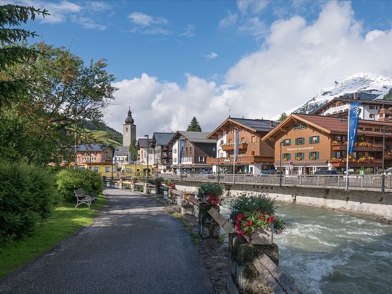 Lech village chalets and church tower lining the Lech river with a snow-dusted peak beyond