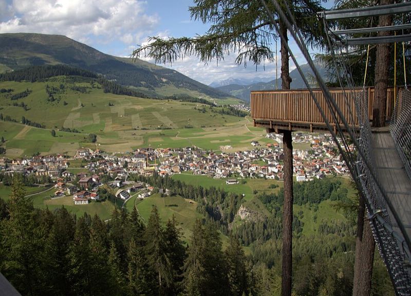 Aerial view of Serfaus village on its sunny high terrace above the Inn valley, seen from a forest viewpoint platform