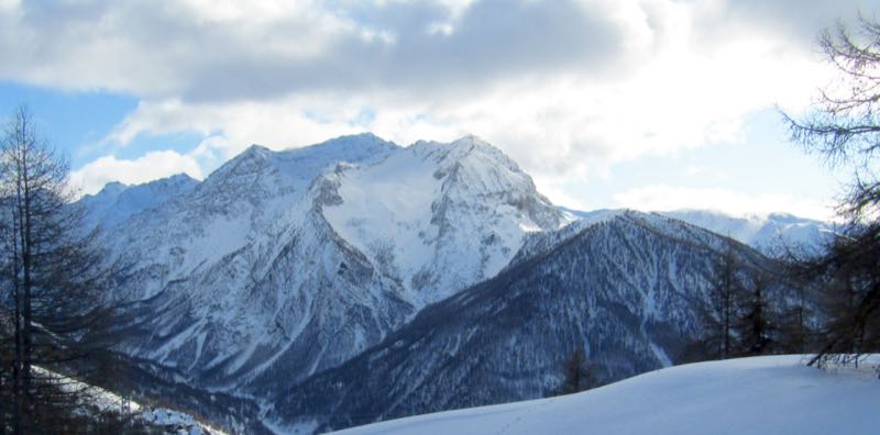 A snow-covered rock peak seen across a valley from a ski run