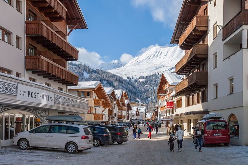Snowy village street in Serfaus lined with chalets and hotels, with a snow-capped mountain rising behind