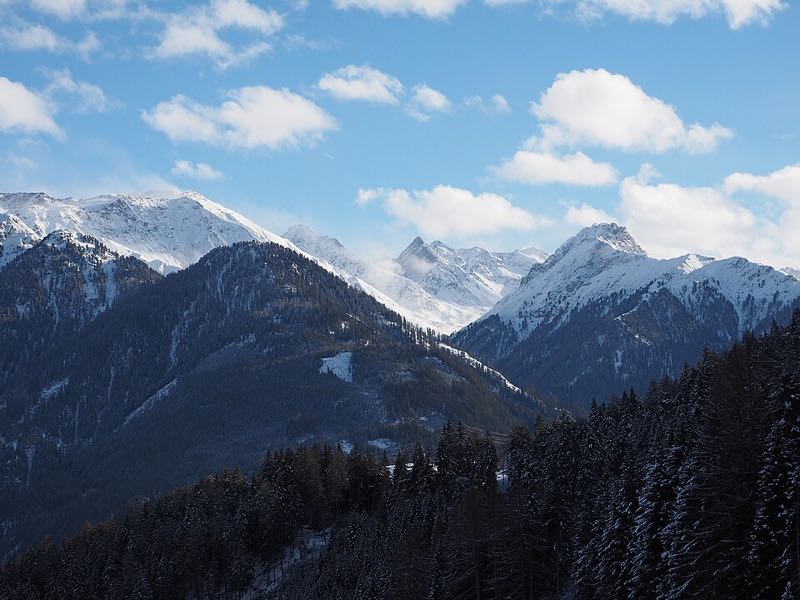Snow-covered alpine peaks and forested slopes above Serfaus under a blue winter sky