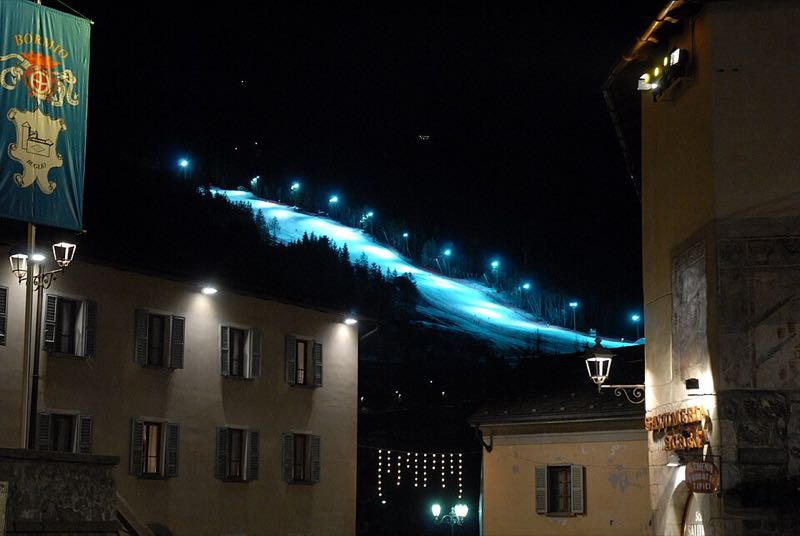 The floodlit Pista Stelvio race slope glowing above the town of Bormio at night